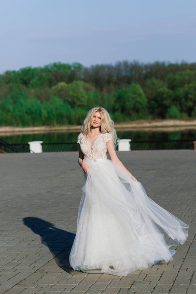 Minsk, Bělorusko - 5.05.2020. Mladá atraktivní blondýnka nevěsta s kudrnatými vlasy procházky v parku a s úsměvem, koncept svatby - Fotografie, Obrázek