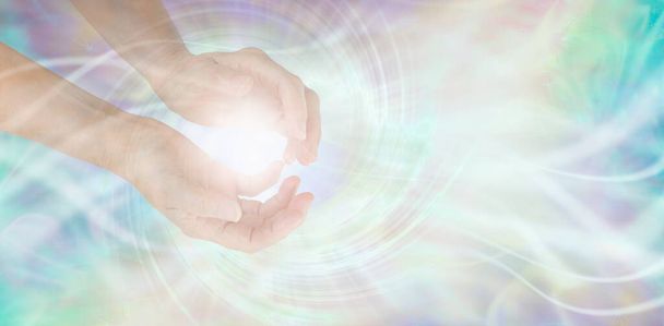 Sensing Vortex healing energy with hands - female cupped hands with a white spirating vortex energy formation and pale pink blue grey misty ethereal energy field background with copy space.  - Foto, Imagen
