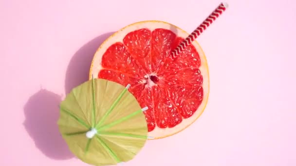 Γκρέιπφρουτ (πορτοκαλί) περιστρέφεται με μια ομπρέλα κοκτέιλ στο φως του ήλιου σε ένα χρωματιστό κίτρινο φόντο. Χυμοί φρούτων, χαλάρωση, τροπικές περιοχές και έννοια χαλάρωσης. - Πλάνα, βίντεο