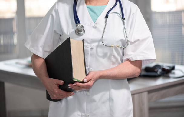 Portrait of female doctor standing and holding a medical textbook - Photo, Image