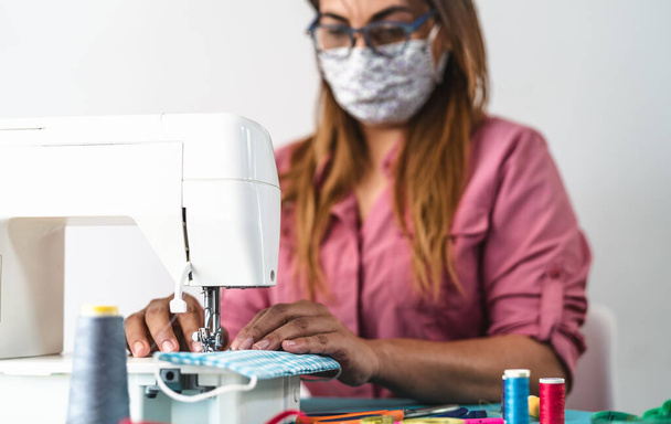 Volwassen vrouw werkt met naaimachine doen zelfgemaakte medische masker voor het voorkomen en stoppen van corona virus verspreiden - Textiel naaister en gezondheidszorg mensen concept - Foto, afbeelding