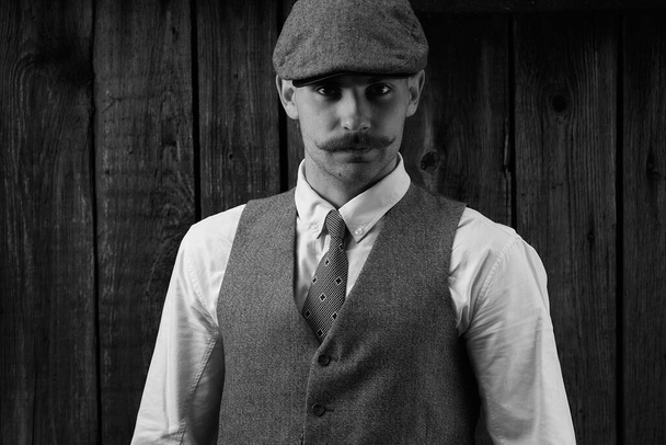 Retro retrato de un tipo con bigote en camisa, chaleco y corbata con gorra
. - Foto, Imagen