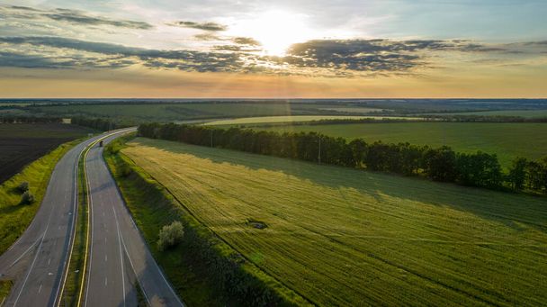 Aerial view photo of the road amid field. Flight over highway amid meadow on summer sunny day. Beautiful countryside landscape scenery from drone view. - Fotó, kép