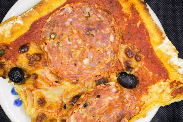 suggestiva immagine di una pizza fatta in casa con salumi piccanti, olive nere, pomodori e mozzarella - Foto, immagini