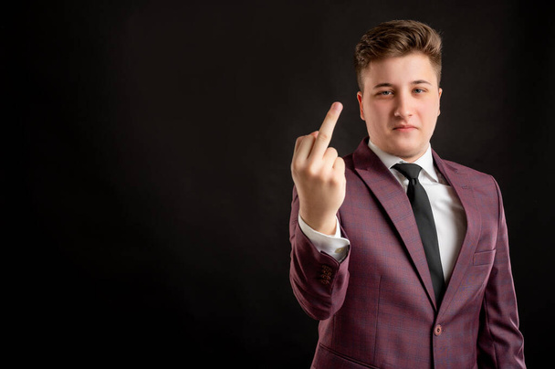 Law student with blond hair dressed in burgundy jacket, white shirt and black tie showing fuck you posing on isolated black background with copy space advertising area - 写真・画像