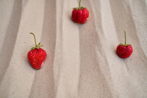 three ripe red strawberries lie on the sand in the desert. High quality photo - Photo, Image