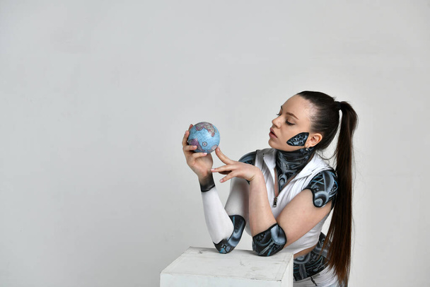 girl in a robot suit plays with a model of the Earth and tries to eat it - Fotoğraf, Görsel