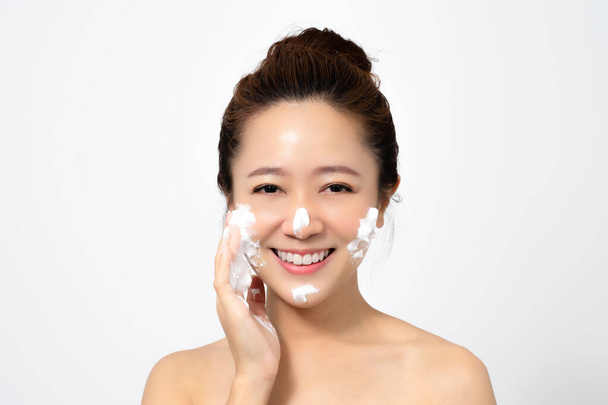 Hermosa mujer asiática está utilizando una espuma facial para lavar los cosméticos de su cara sobre un fondo blanco
. - Foto, imagen