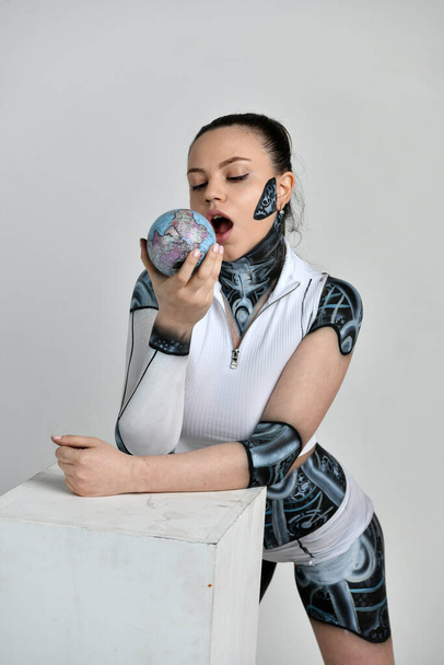 meisje in een robot pak speelt met een model van de aarde en probeert te eten - Foto, afbeelding