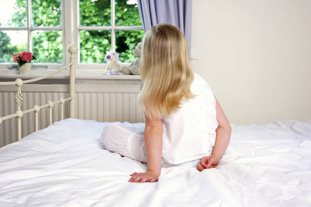 Back shot of a girl in white dress sitting on the bed - Foto, Imagen