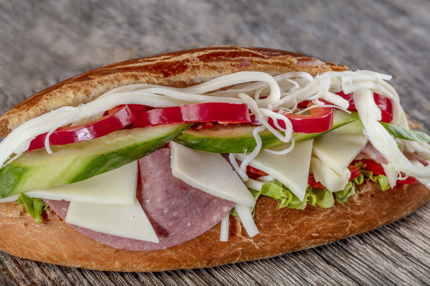 Sandwich met ham, kaas, tomaten, sla, komkommers en uien op donkere houten ondergrond. - Foto, afbeelding