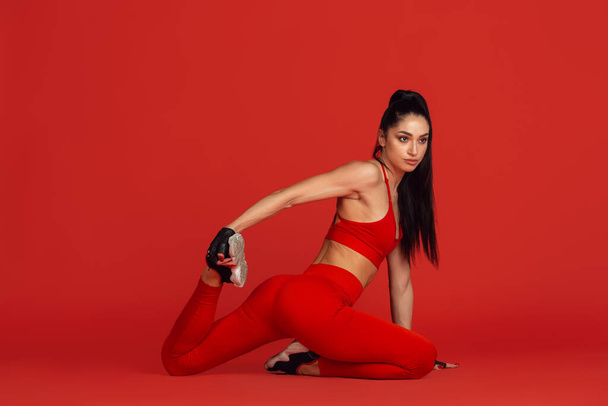 Beautiful young female athlete practicing on red studio background, monochrome portrait - Fotó, kép