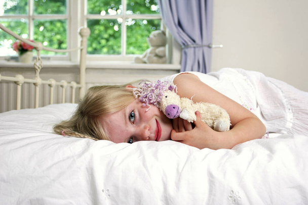 A girl lying on the bed hugging a teddy bear - Valokuva, kuva