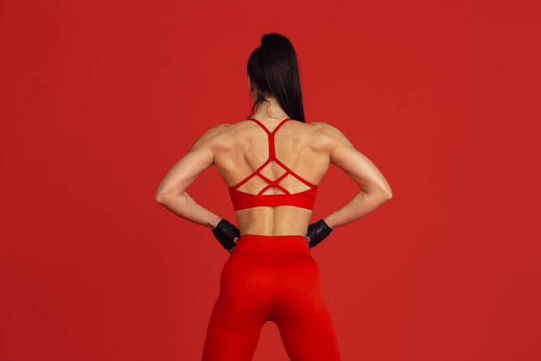 Beautiful young female athlete practicing on red studio background, monochrome portrait - Photo, image