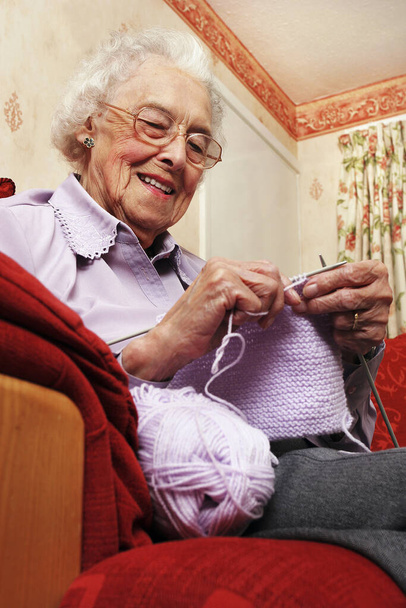 An old bespectacled lady sitting on the couch knitting - Foto, imagen