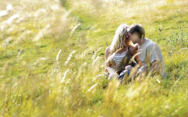 Una pareja sentada en la hierba besándose - Foto, Imagen