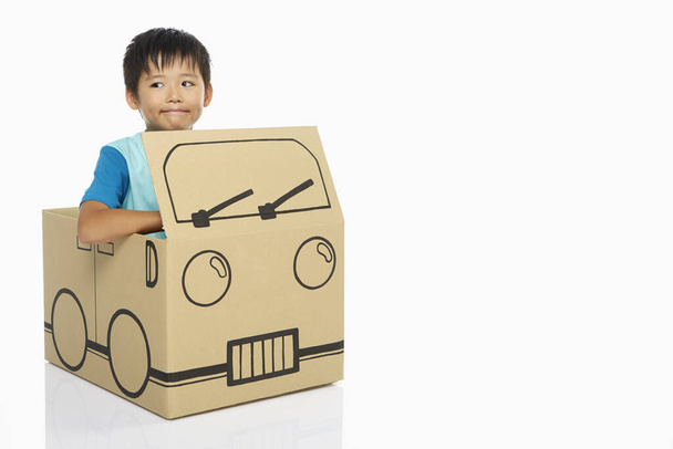 Boy sitting inside a cardboard bus - Photo, image