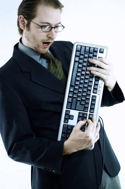 A bespectacled man holding a computer keyboard like he is playing a guitar - Φωτογραφία, εικόνα