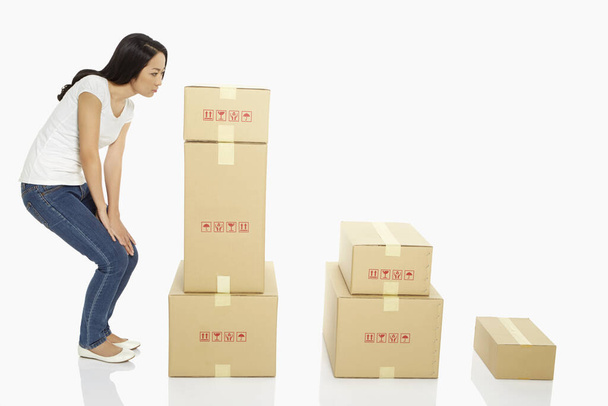 Woman standing beside a stack of cardboard boxes, contemplating - Foto, immagini
