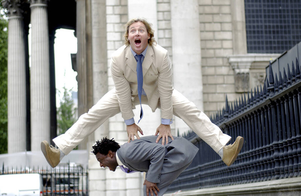 A man in business suit jumping over another man who is bending down - Фото, зображення