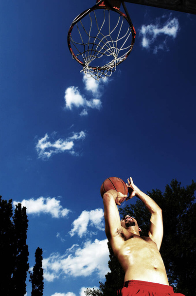 Bottom view of a man trying to shoot a ball into the hoop - Photo, image