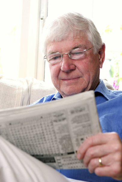 A bespectacled old man sitting on the couch reading newspaper - Fotoğraf, Görsel
