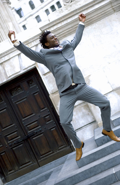 Un hombre afroamericano en traje de negocios de puntillas con las manos en alto
 - Foto, Imagen