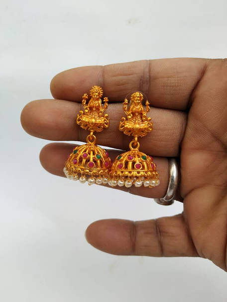 Closeup of Holding Goddess Lakshmi Estátuas no anel de orelha artesanal tradicional dourado com pedras e pedras preciosas isoladas no fundo branco
 - Foto, Imagem