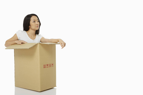 Woman sitting inside of a cardboard box, smiling - Foto, imagen