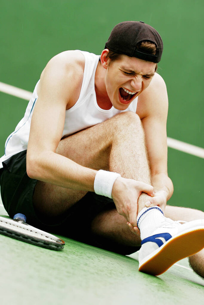 A tennis player screaming in pain after he sprained his leg - Foto, Imagen
