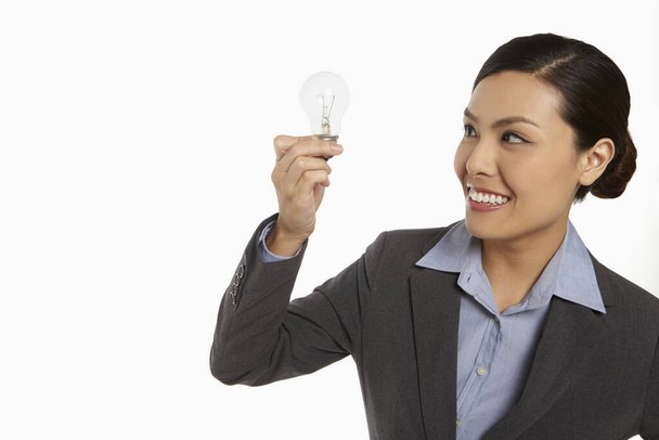Businesswoman smiling and holding up a light bulb - Foto, imagen