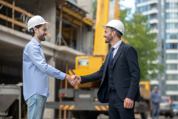 Building supervisor shaking hands with foreman on building site - 写真・画像