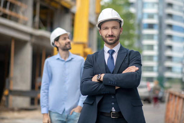 Building supervisor standing with folded arms, foreman looking sideways behind him - Foto, afbeelding