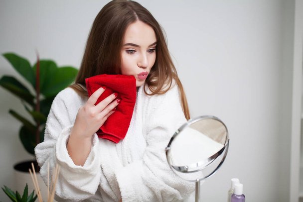 Reiniging van de gezichtshuid, jonge vrouw met rode handdoek in de buurt van de gezichtshuid na het wassen gezicht - Foto, afbeelding