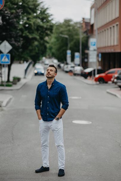 Young man stands in jeans and shirt at street against background of building. - Foto, imagen