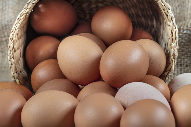 Jajka. Kilka świeżych jaj kurzych w słomkowym koszu na drewnianym tle. Koncepcja zdrowego odżywiania. - Zdjęcie, obraz