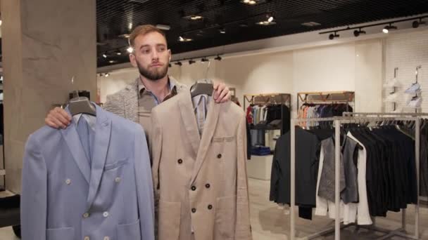 Stilvoller Mann mit Bart wählt Jacke in Herrenbekleidungsgeschäft. - Filmmaterial, Video