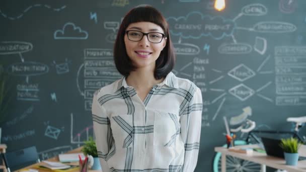 Portrait of cute girl standing in creative office and smiling looking at camera - Video