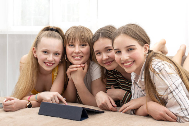 Shot of smiling girlfriends lying on the sofa and happily watching something interesting on the tablet.  Happy youth concept - Foto, afbeelding