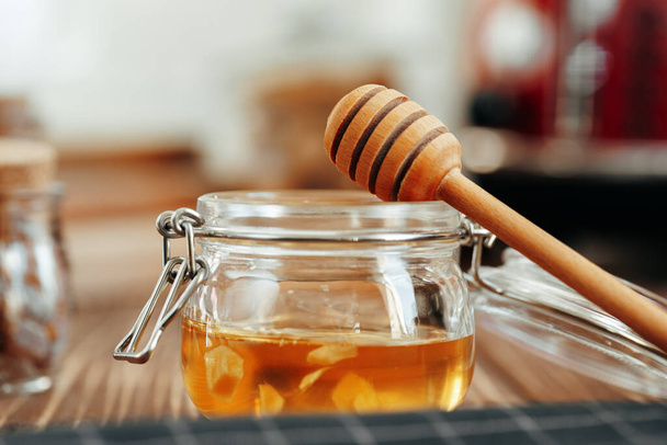 Glass jar of honey on wooden kitchen table - Foto, imagen