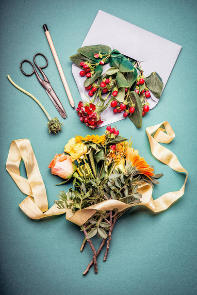 Autumn flowers bunch with envelop , shears , pencil and flowers on blue workspace table background, top view. Creative Flowers arrangement.  Invitation , greeting and holiday, concept - Foto, afbeelding