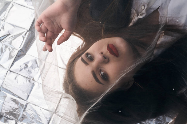 Krásný make-up baculaté dívky leží na zlaté fólii pod tyl tkaniny. - Fotografie, Obrázek