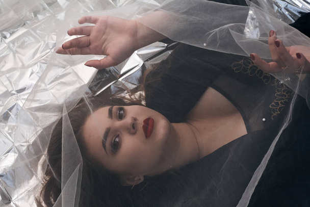 Beautiful makeup of a chubby girl lies on a gold foil under a tulle fabric. - Foto, afbeelding