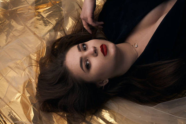 Beautiful makeup of a chubby girl lies on a gold foil. - 写真・画像
