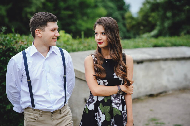 Loving happy couple. Beautiful brunette in dress and young man in white shirt, pants with suspenders walking through city streets. - Photo, Image