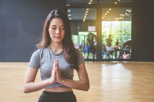 Young attractive woman practicing yoga with closed eyes relaxing, sitting in Padmasana exercise, practicing yoga, attractive sporty girl wearing gray sportswear working out at home or in yoga studio - Photo, Image