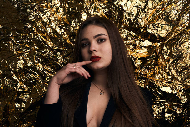 Stylish chubby girl posing in a black jacket on a gold background. - Foto, afbeelding