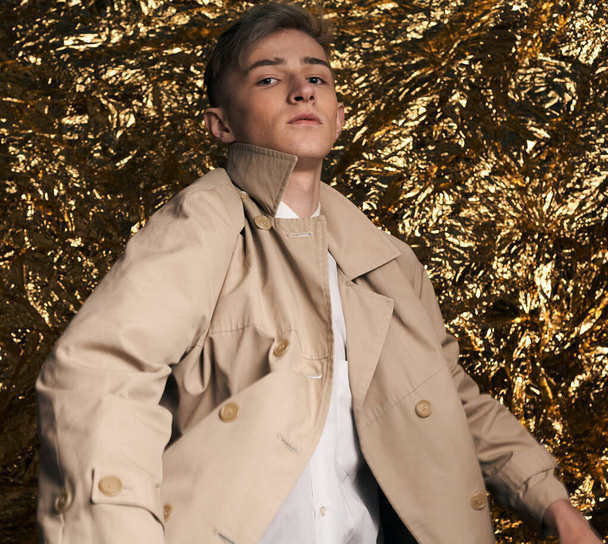 Stylish guy in a beige coat and a white shirt on a gold background. - Photo, Image