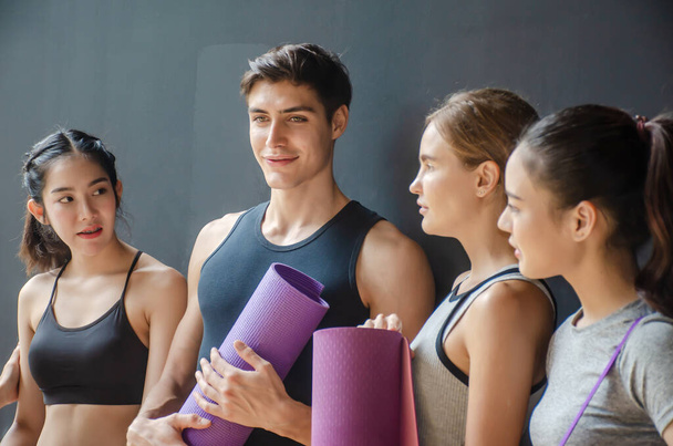 Group of young sporty people with fitness yoga exercise mats standing beside black wall.Students taking a rest from fitness activity, time to recover strength, waiting for a lesson to start in loft studio,Selective focus is man - Foto, immagini