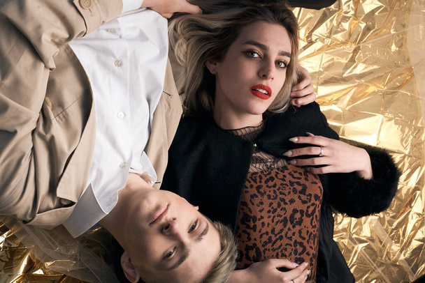 Stylish couple posing on a golden background from a foil lying. - Foto, afbeelding